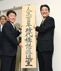 出典：人生100年時代構想推進室の看板を掛ける安倍晋三内閣総理大臣と茂木敏充経済再生担当大臣（2017年9月）